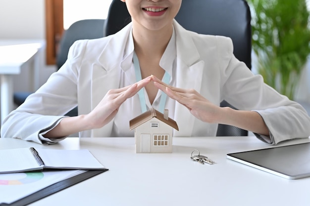 Souriante jeune femme main protégeant le modèle de maison. Concept immobilier d'assurance ou de prêt.