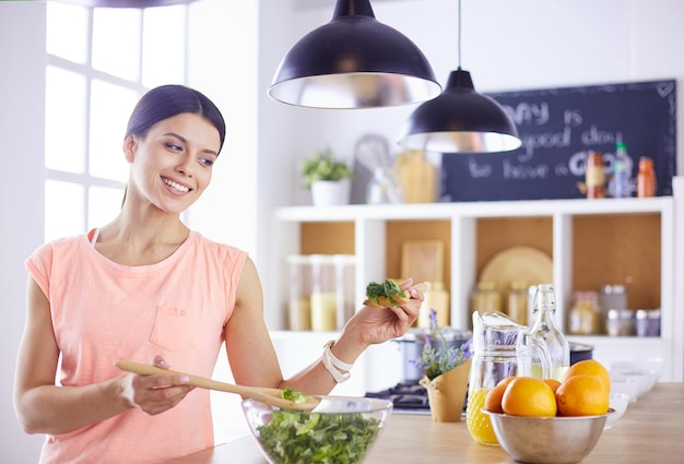 Souriante jeune femme mélangeant une salade fraîche dans la cuisine