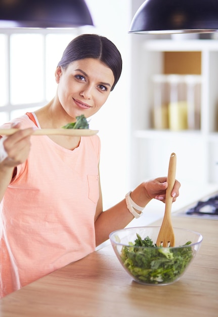 Souriante jeune femme mélangeant une salade fraîche dans la cuisine