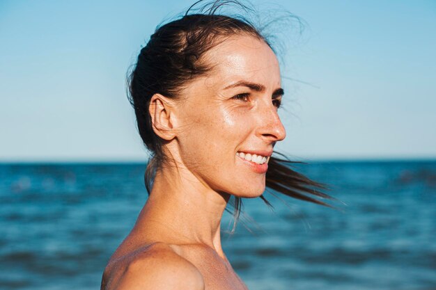 Souriante jeune femme à la mer regarde sur le côté.