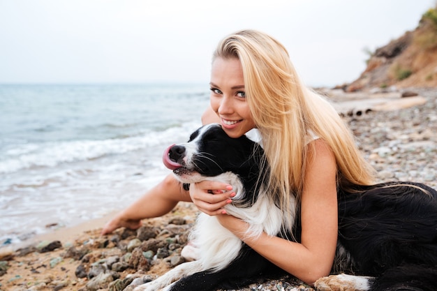 Souriante jeune femme mignonne avec son chien sur la plage