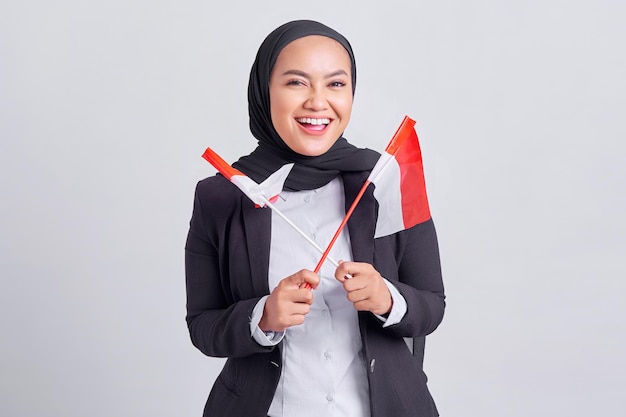 Souriante jeune femme musulmane asiatique tenant le drapeau indonésien et célébrant le jour de l'indépendance indonésienne isolé sur fond blanc