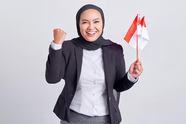 Souriante jeune femme musulmane asiatique tenant le drapeau indonésien et célébrant le jour de l'indépendance indonésienne isolé sur fond blanc