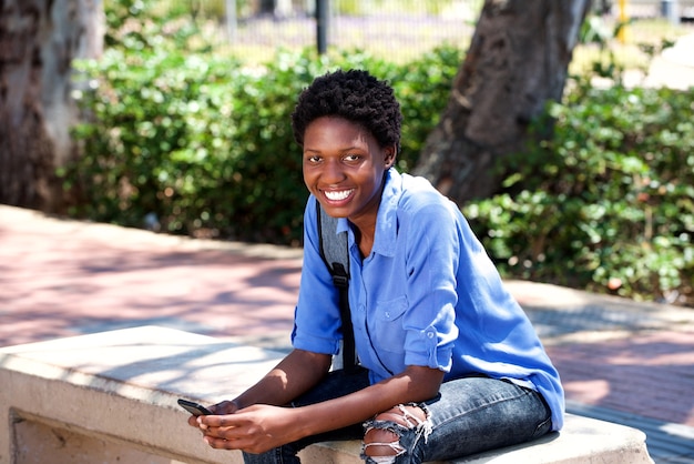 Souriante Jeune Femme Noire Assise à L'extérieur Avec Un Téléphone Portable