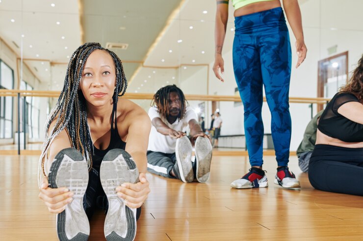 Photo souriante jeune femme noire avec des dreadlocks assis sur le sol et s'étendant vers l'avant en touchant la pointe des pieds
