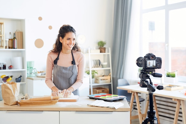 Souriante jeune femme pétrir la pâte pour les cupcakes lors du tournage vidéo pour son blog culinaire