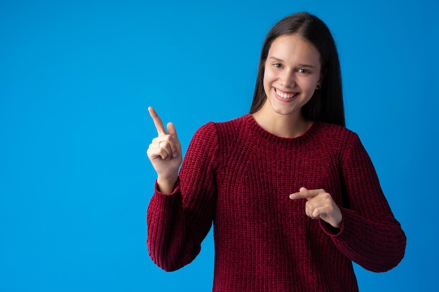 Souriante jeune femme pointant vers l'espace de copie sur fond bleu