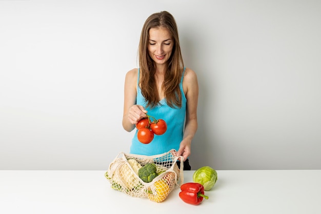 Souriante jeune femme posant des légumes achetés sur la table