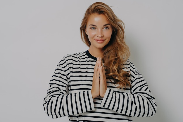 Souriante jeune femme positive avec les mains jointes dans le geste de namaste et souriant à la caméra