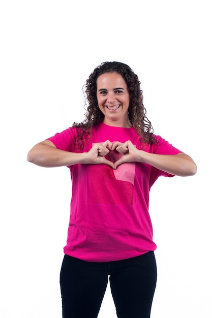 Souriante jeune femme positive avec t-shirt rose en forme de coeur avec les mains.