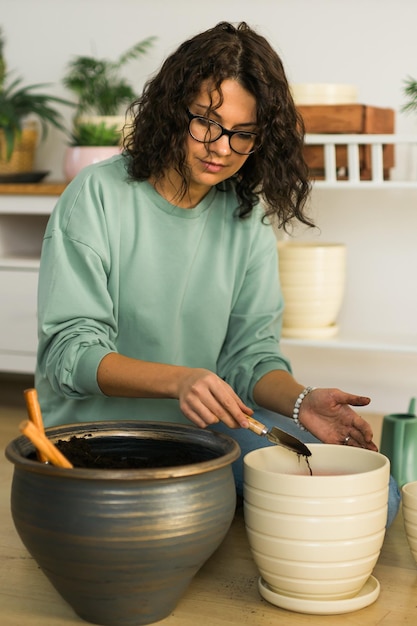 Photo souriante jeune femme et pot avec plante travail heureux dans un jardin intérieur ou un bureau à domicile confortable avec différentes plantes d'intérieur heureuse jardinière ou fleuriste du millénaire prend soin de la fleur domestique