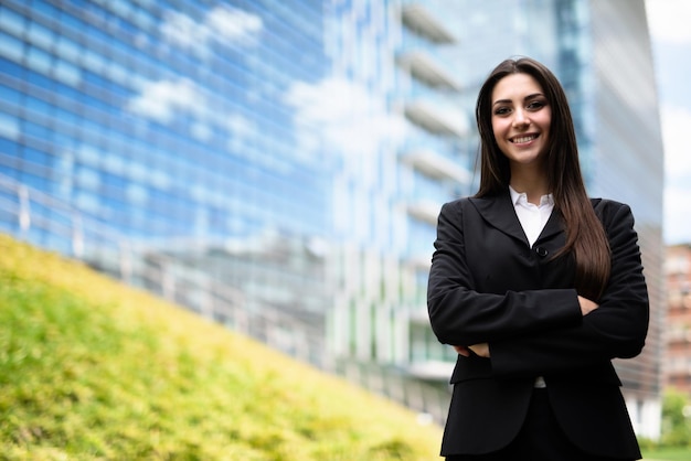 Souriante jeune femme près d'un champ d'herbe et d'un immeuble de bureaux en verre