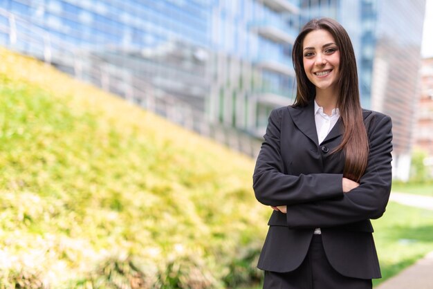 Souriante jeune femme près d'un champ d'herbe et d'un immeuble de bureaux en verre