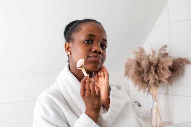 Souriante jeune femme regardant la caméra masser la peau par rouleau