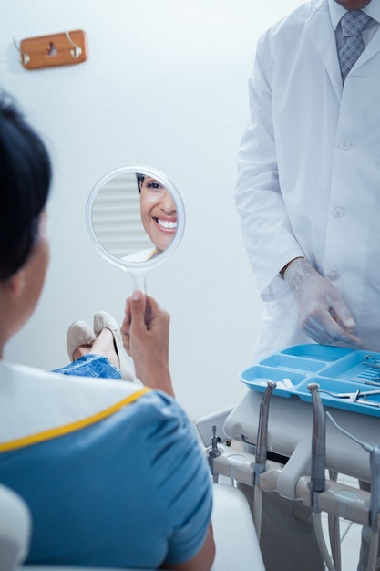 Souriante jeune femme regardant le miroir dans la chaise de dentiste