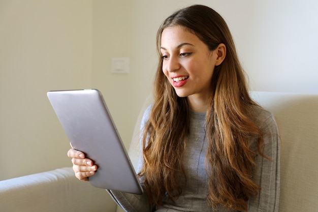 Souriante jeune femme regardant l'ordinateur tablette pc assis à la maison