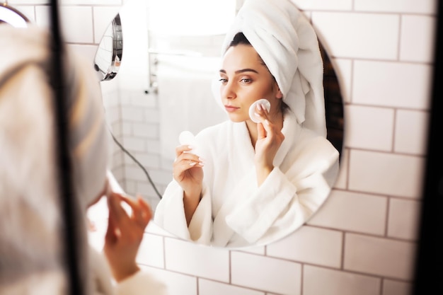 Souriante jeune femme se lavant le visage avec une éponge nettoyante pour le visage dans la salle de bain.