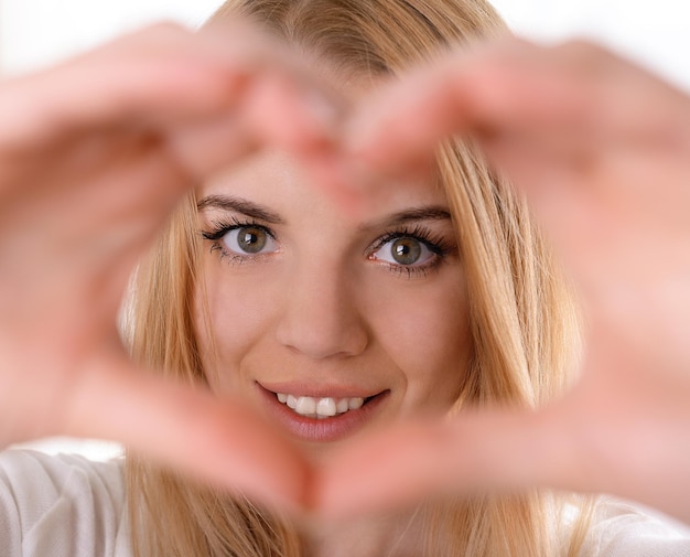 Souriante jeune femme séduisante fait coeur à l'aide des doigts