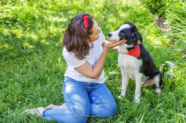 Souriante jeune femme séduisante jouant avec mignon chiot border collie dans le jardin d'été ou le parc de la ville en plein air