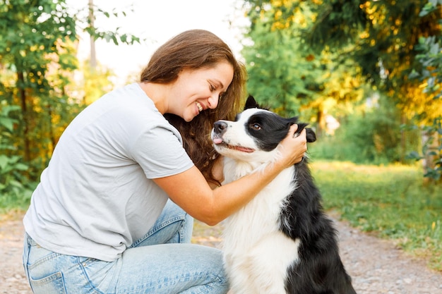 Souriante jeune femme séduisante jouant avec un mignon chiot border collie sur fond extérieur d'été. Fille tenant embrassant un ami chien étreignant. Concept de soins pour animaux de compagnie et d'animaux.