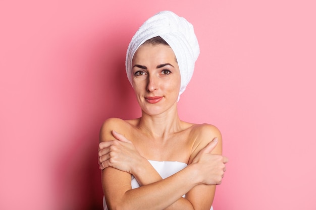 Souriante jeune femme avec une serviette sur la tête sur fond rose.