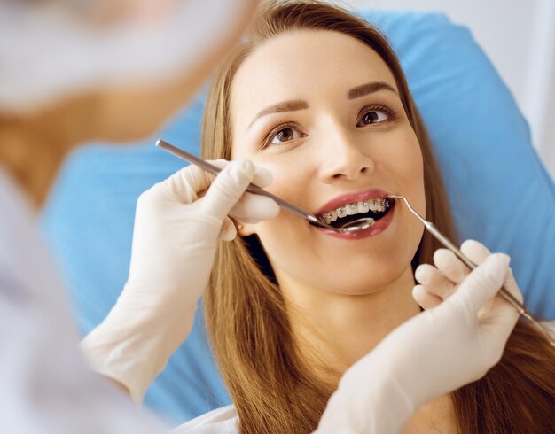 Souriante jeune femme avec des supports orthodontiques examinés par un dentiste à la clinique dentaire. Dents saines et concept de médecine.