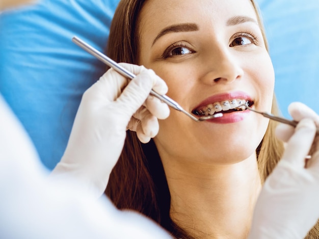 Souriante jeune femme avec des supports orthodontiques examinés par un dentiste dans une clinique dentaire. Dents saines et concept de soins médicaux.