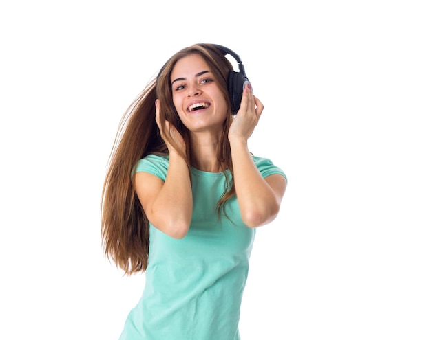 Souriante jeune femme en T-shirt bleu écoutant de la musique dans un casque noir sur fond blanc