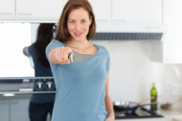Souriante jeune femme tenant un couteau dans la cuisine