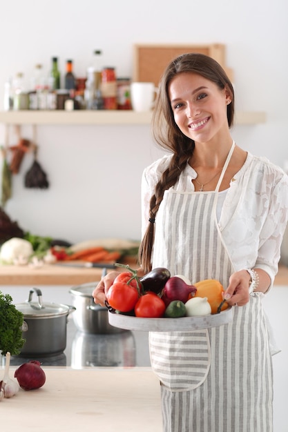 Souriante jeune femme tenant des légumes debout dans la cuisine