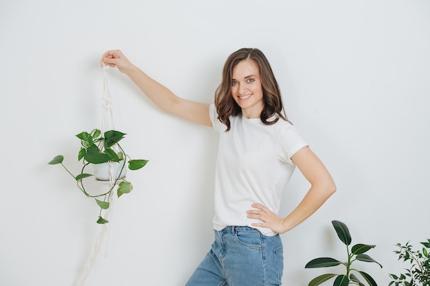 Souriante jeune femme tenant une plante en pot dans une bretelle en macramé