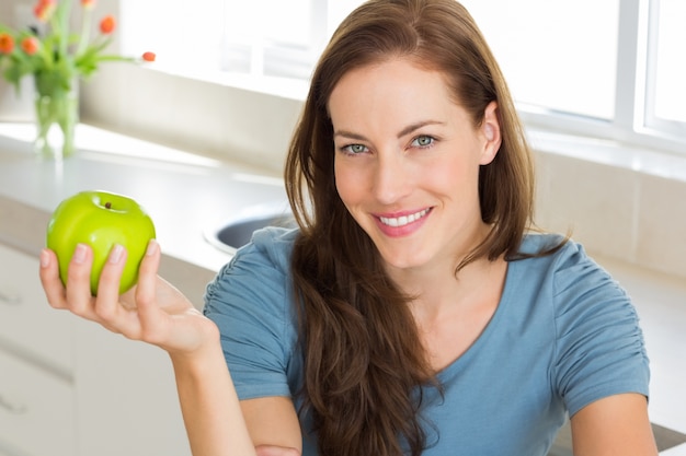 Souriante jeune femme tenant une pomme dans la cuisine