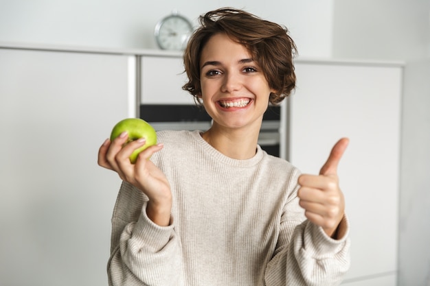 Souriante jeune femme tenant une pomme verte dans la cuisine