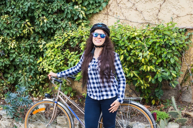 Souriante jeune femme tenant un vélo dans le parc de la ville