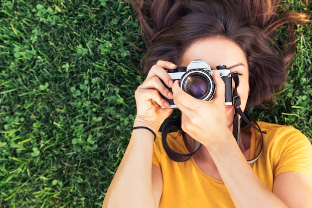 Souriante jeune femme utilisant un appareil photo pour prendre des photos dans le parc.