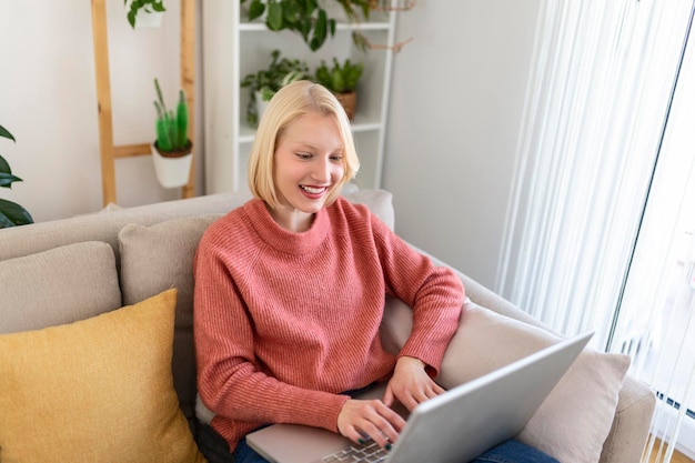 Souriante jeune femme utilisant un ordinateur portable à la maison, regardant l'écran, bavardant, portant un casque sans fil ayant une vidéoconférence. tutorat de formateur d'entreprise par webcam, formation en ligne, concept de e-coaching