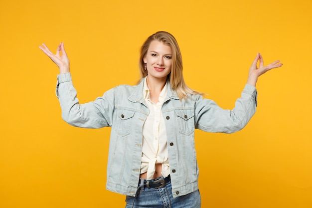 Souriante jeune femme en vêtements décontractés en denim regardant la caméra, tenir la main dans un geste de yoga relaxant méditant isolé sur fond orange jaune en studio. Concept de style de vie des gens. Maquette de l'espace de copie.