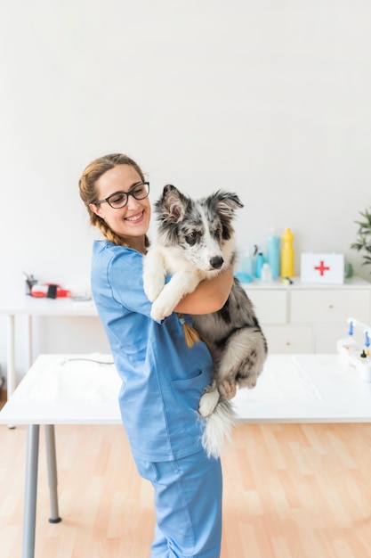 Photo souriante jeune femme vétérinaire portant le chien en clinique