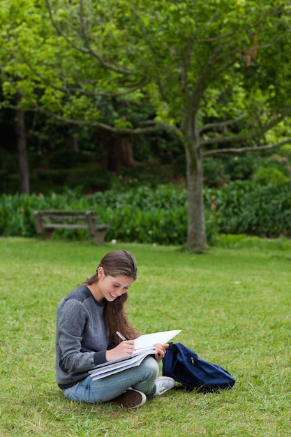 Souriante jeune fille écrit sur son carnet tout en étant assis sur l&#39;herbe