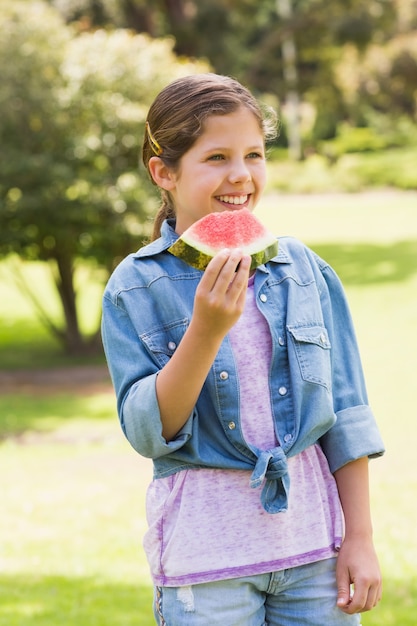 Souriante jeune fille mangeant melon d&#39;eau dans le parc