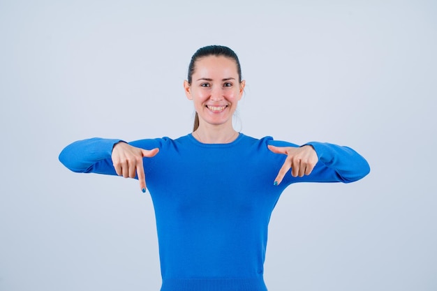 Souriante jeune fille pointe vers le bas avec les index sur fond blanc