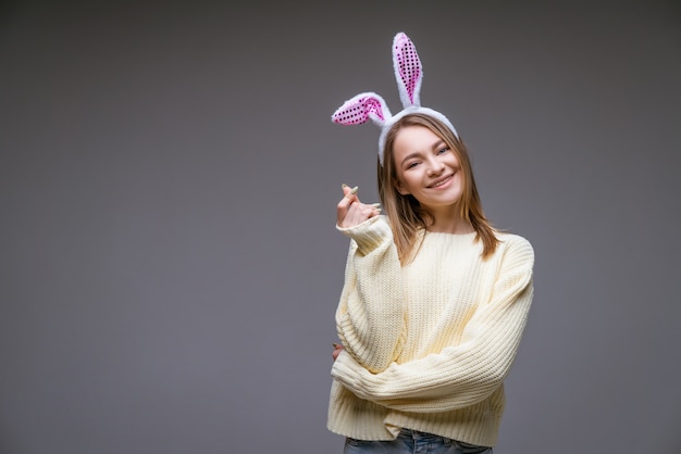 Souriante jeune fille de race blanche, blonde aux oreilles de lapin, montre un mini coeur avec les doigts