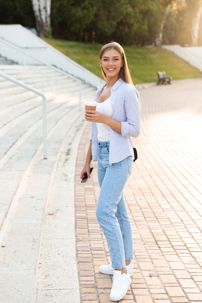 Souriante jeune fille avec sac à dos tenant du café à emporter