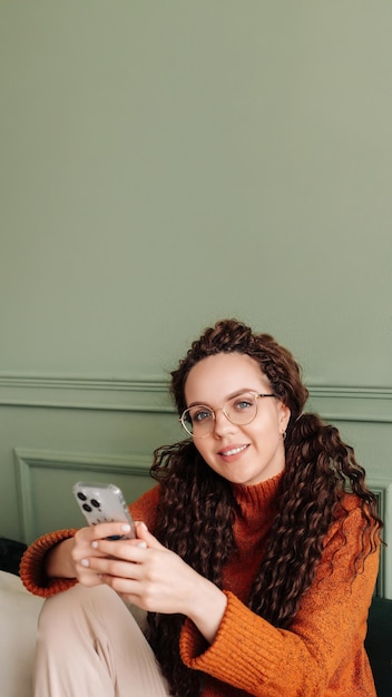 Souriante jeune jolie femme assise à la maison à l'aide d'applications sur la technologie de téléphone portable heureuse dame tenant