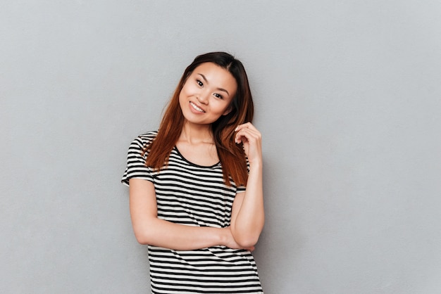 Souriante jeune jolie femme debout sur un mur gris.