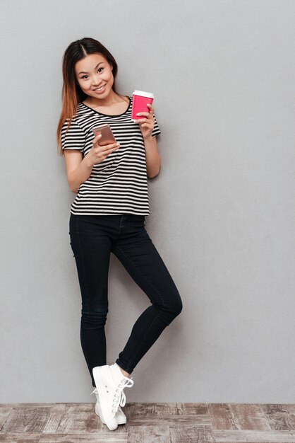 Souriante jeune jolie femme debout sur un mur gris.