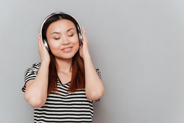 Souriante jeune jolie femme écoutant de la musique avec des écouteurs