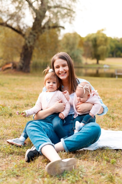 Souriante jeune mère tenant ses deux petites filles de bébé en plein air
