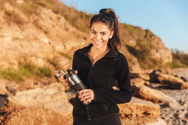 Souriante jeune sportive debout au bord de la mer