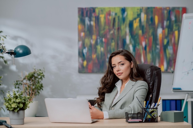 Souriante jolie brune aux yeux noirs en veste est assise dans une chaise confortable